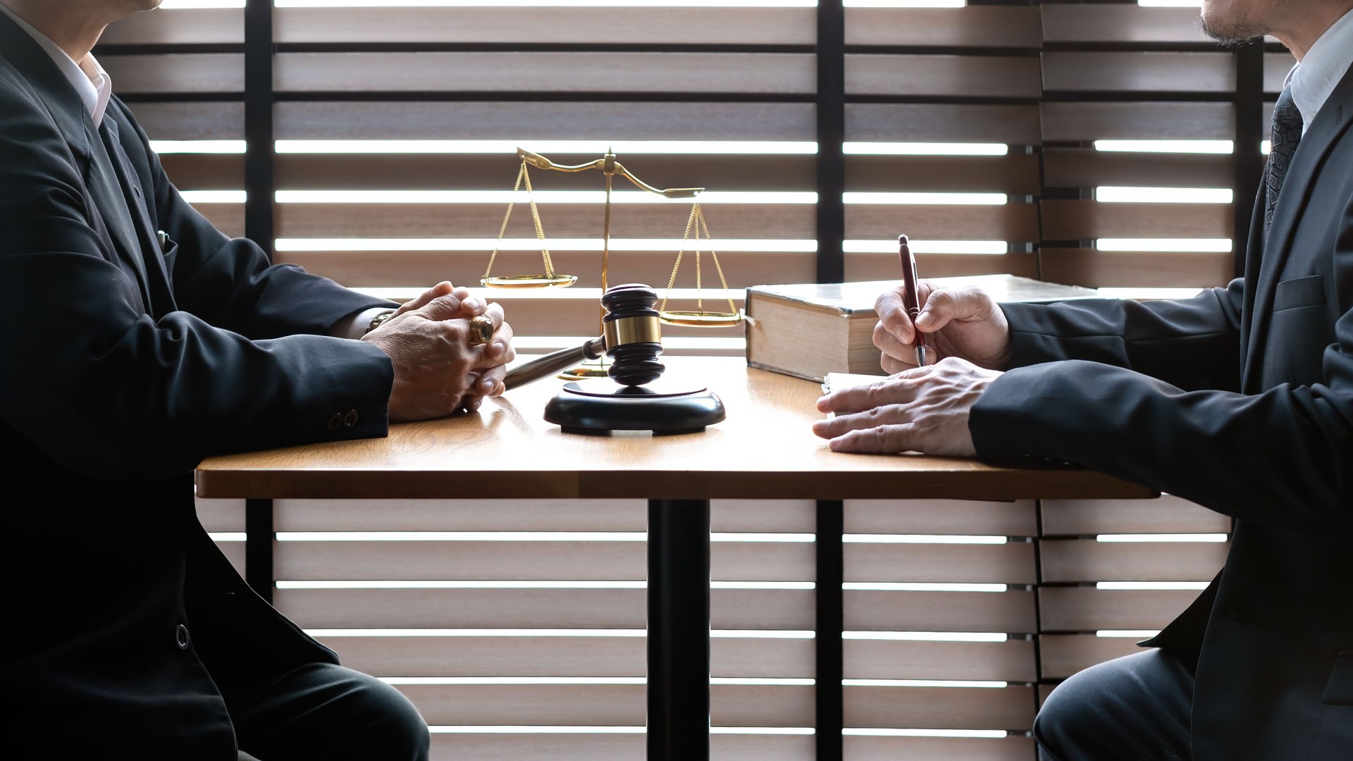 Two business professionals discussing legal matters at desk with gavel, justice scale, and law book, law consultation, corporate agreements, and professional judgment